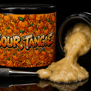 Sour Tangie gas extract in loud orange-branded jar with strawberry graphics and golden concentrate sitting in black container next to metal dab tool